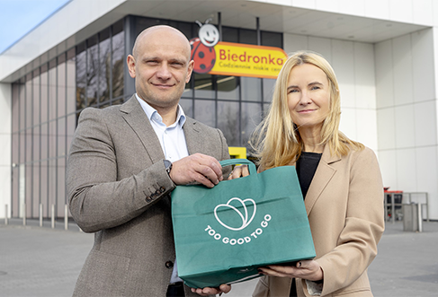Two people in front of a Biedronka store holding a Too Good to Go bag. (photo)