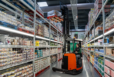An employee using a fork lift to lift a palette onto a high storage shelf. (photo)