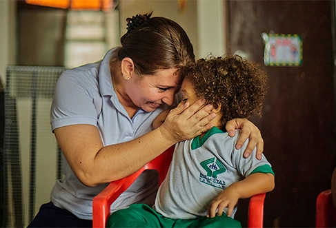 A woman in a light blue polo shirt hugs a child and holds his face. (photo)