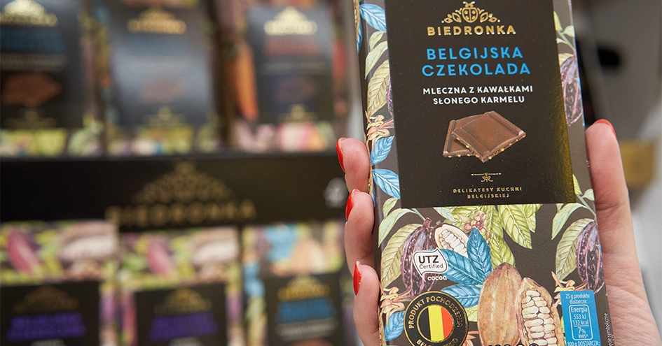 A hand holding a bar of Biedronka chocolate in front of a shelf with further chocolate bars (photo)