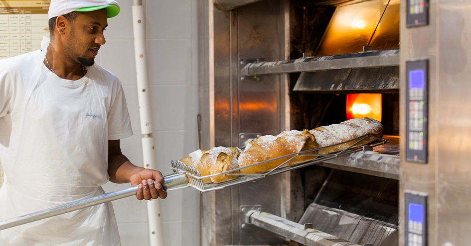 Baker pulling fresh bread loaves out of the oven (photo)