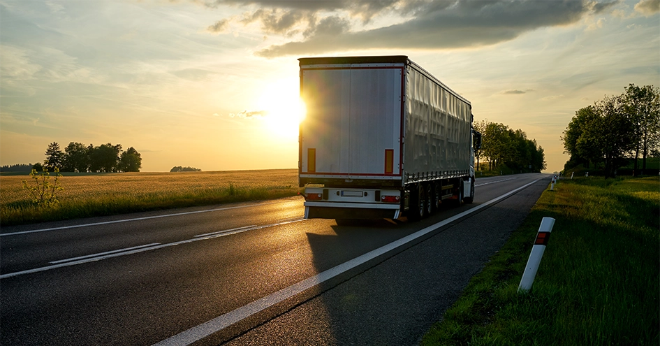 A truck driving on a road photographed from behind with the sun setting in the background (photo)