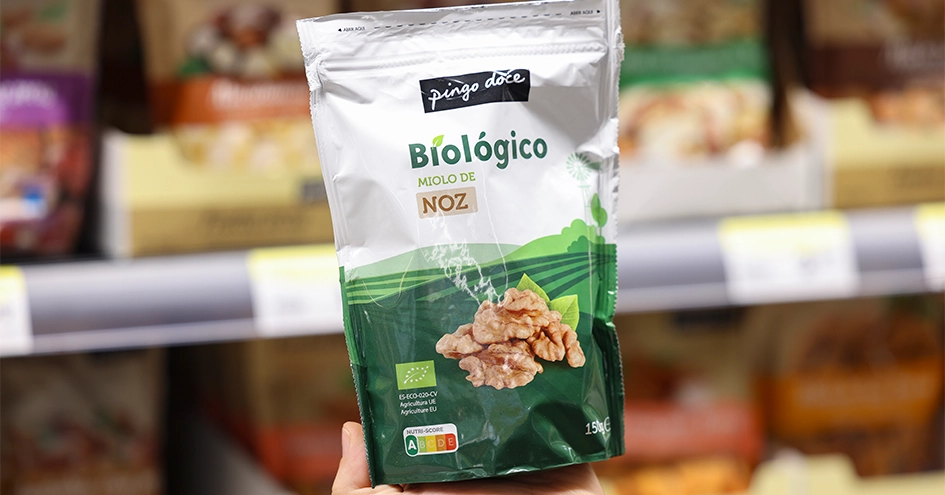 Hand holding a bag of walnuts in front of a shelf with various nuts (photo)