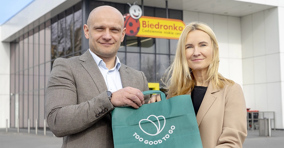 Two people in front of a Biedronka store holding a Too Good to Go bag (photo)