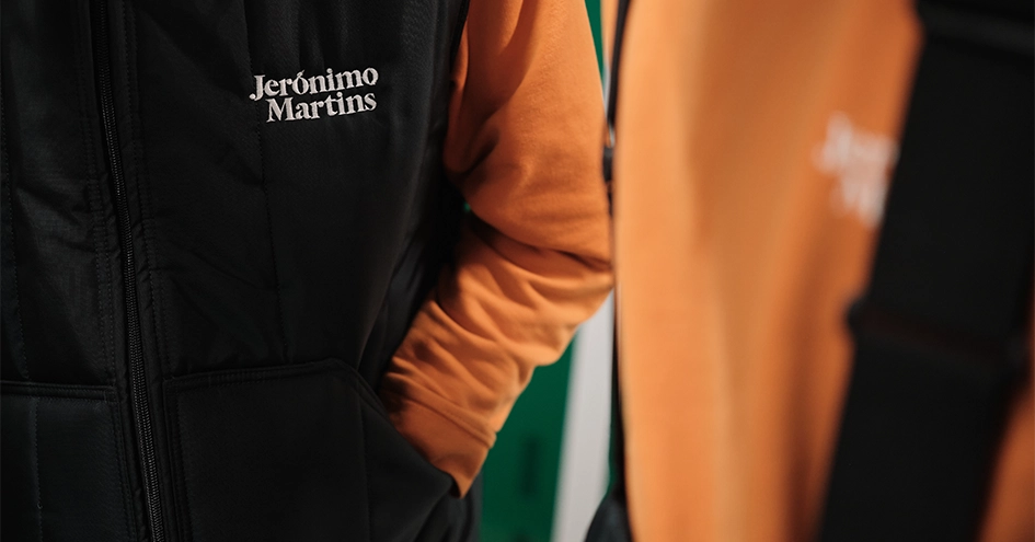 Close-up of employees wearing orange sweaters and dark blue vests with the Jerónimo Martins logo (photo)