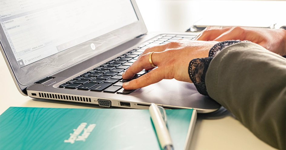 Close-up of a person typing on a notebook with a Jerónimo Martins branded writing notepad in the foreground (photo)