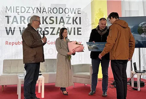 A woman and two men hand over prizes (a cheque and a bouquet of flowers) to the winner at an award ceremony (photo)