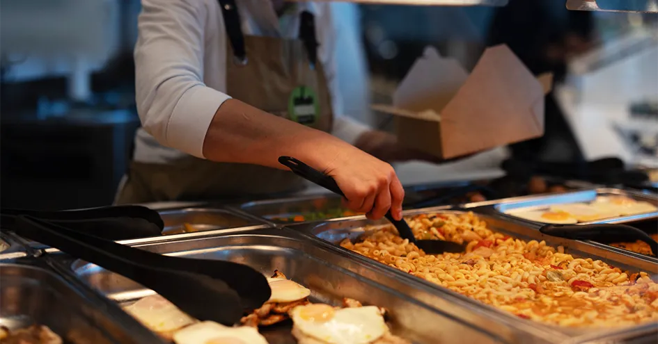 A Comida Fresca employee placing a pasta dish in a cardboard takeaway box (photo)