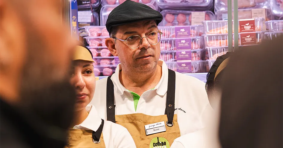 A group of Pingo Doce employees with Comida Fresca aprons standing in front of the refrigerated meat section. The photo is taken over the shoulder of two of the employees (photo)