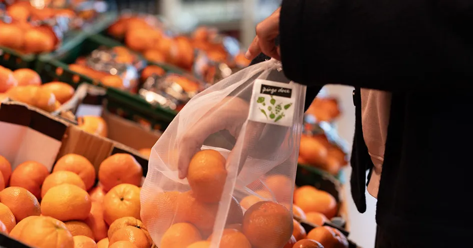 Close-up showing a person picking mandarins in a store and placing them in a reusable bag (photo)