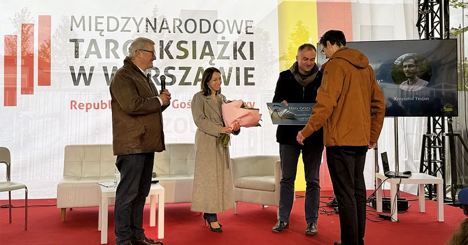 A woman and two men hand over prizes (a cheque and a bouquet of flowers) to the winner at an award ceremony (photo)