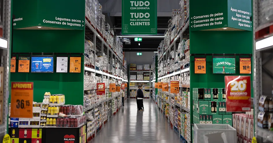 Aisle for canned food in a Recheio with customers in the background (photo)