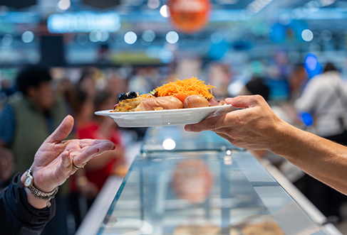Um cliente recebe um tabuleiro cheio de comida por cima de um expositor de vidro.&nbsp; (foto)