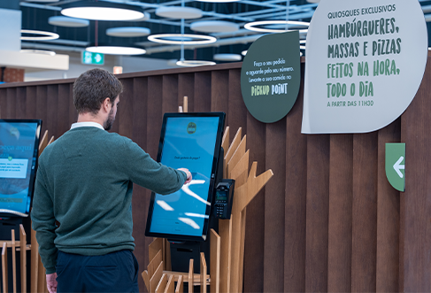 Um cliente com um pulover verde escuro a utilizar um terminal de self-checkout. (foto)
