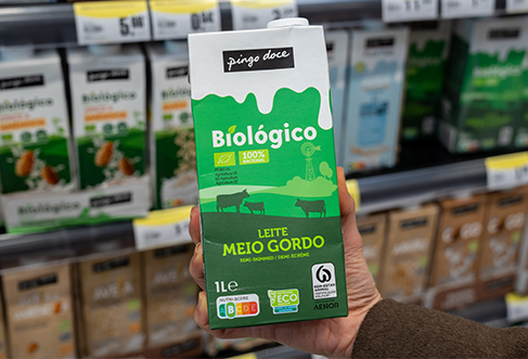 Plano fechado de uma mão a retirar uma garrafa de leite sem lactose de uma prateleira no Pingo Doce (foto)