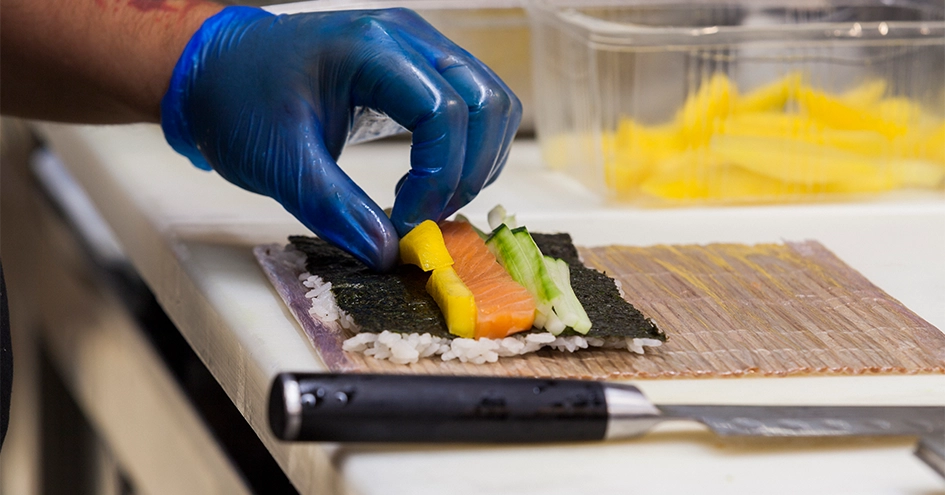 Plano fechado de uma mão a preparar sushi (foto)