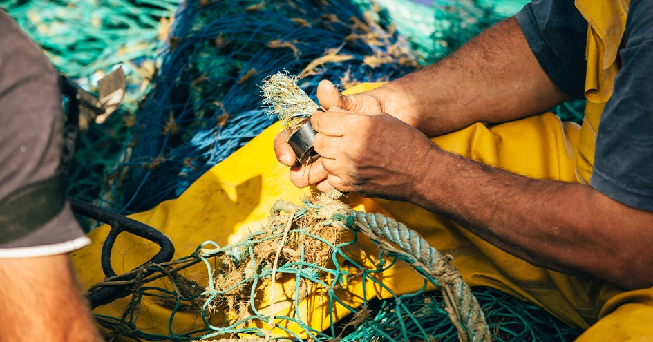 Plano fechado de um pescador a remendar uma rede (foto)