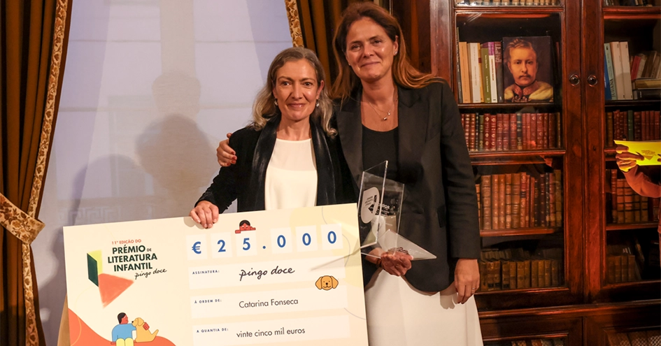 Duas pessoas numa biblioteca a segurar um cheque de mais de 25.000 euros emitido pelo Pingo Doce e um troféu (foto)