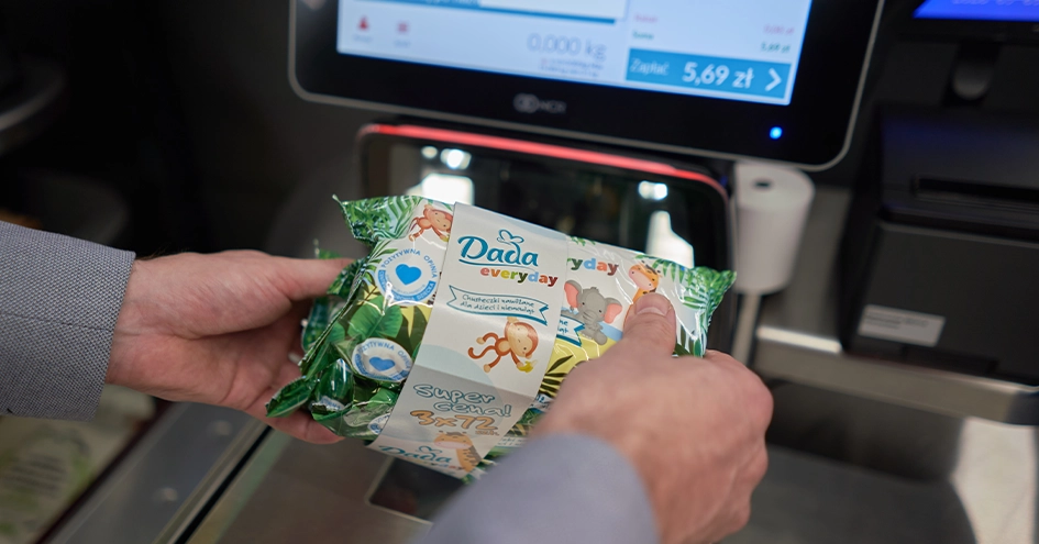 Plano fechado de uma pessoa a fazer o scan de toalhitas Dada numa caixa de pagamento automática com as duas mãos (foto)