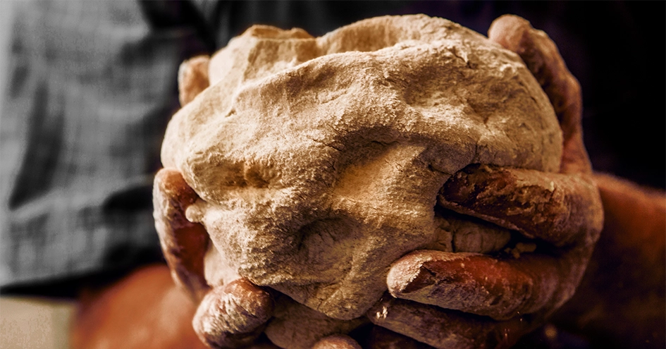 Plano fechado de mãos a segurar em massa de pão (foto)