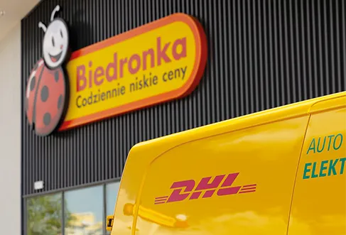 Um carro de entregas da DHL em frente a uma loja Biedronka (foto)