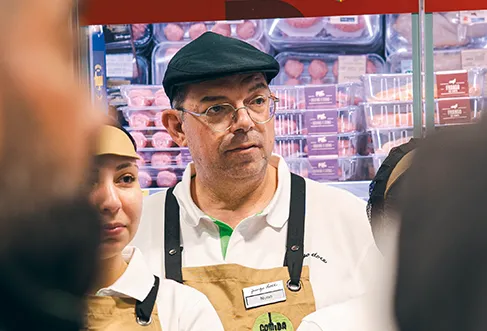 Um grupo de colaboradores do Pingo Doce com aventais Comida Fresca em frente à secção de carne refrigerada. A fotografia foi tirada por cima do ombro de dois dos colaboradores (foto)