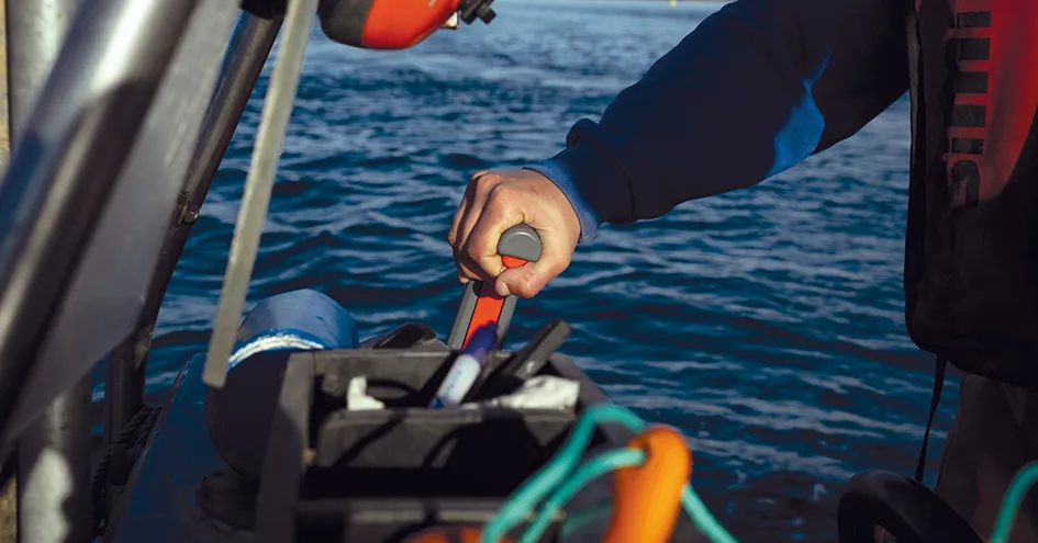 Grande plano a mostrar o braço e a mão de uma pessoa a segurar o leme de um barco (foto)