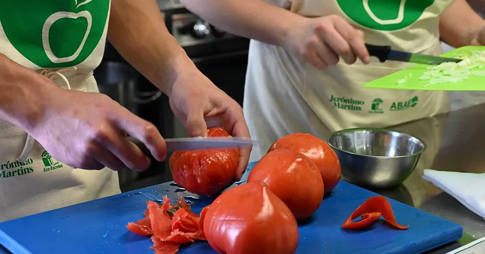 Grande plano de uma pessoa a descascar tomates, enquanto outra corta cebolas à direita (foto)