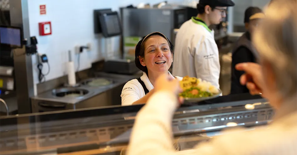 Uma colaboradora entrega um prato com comida a um cliente por cima do balcão (foto)