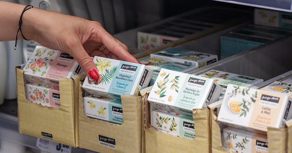 Plano fechado de uma mulher a retirar um sabonete do Pingo Doce de uma prateleira com várias referências de sabonetes. (foto)