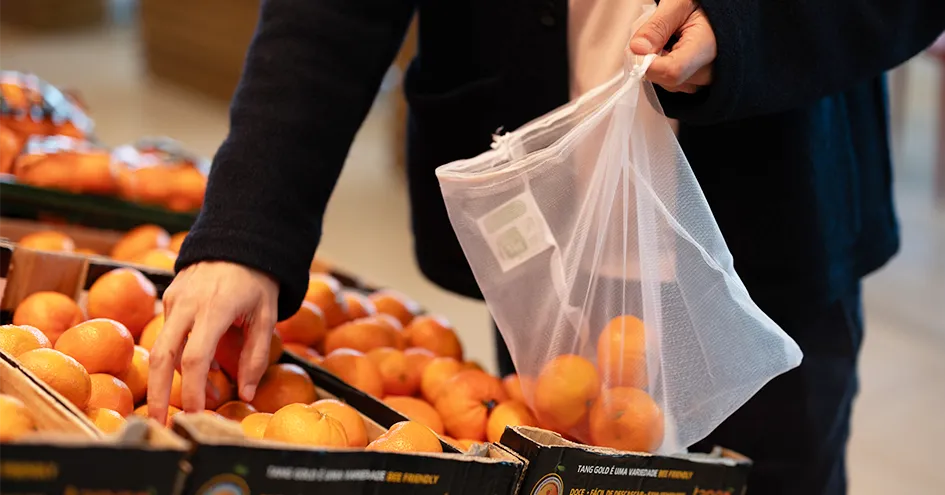 Grande plano a mostrar uma pessoa a escolher tangerinas numa loja e a colocá-las num saco reutilizável (foto)