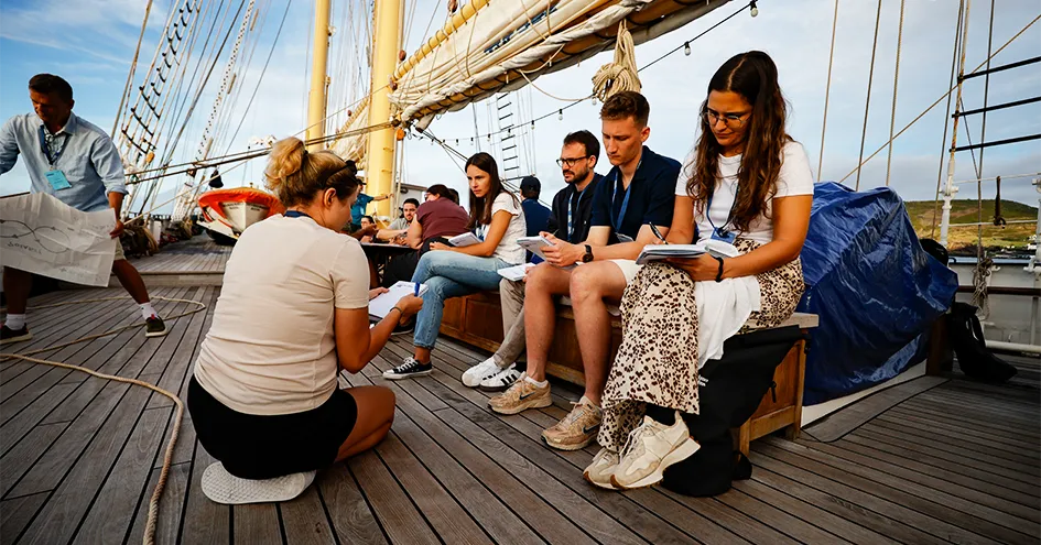 Jovens adultos sentados num banco no navio Santa Maria Manuela a tirar notas (foto)