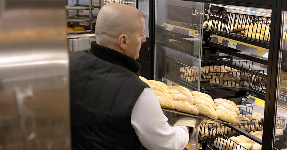 Um colaborador a encher a vitrina da padaria com pães acabados de cozer (foto)